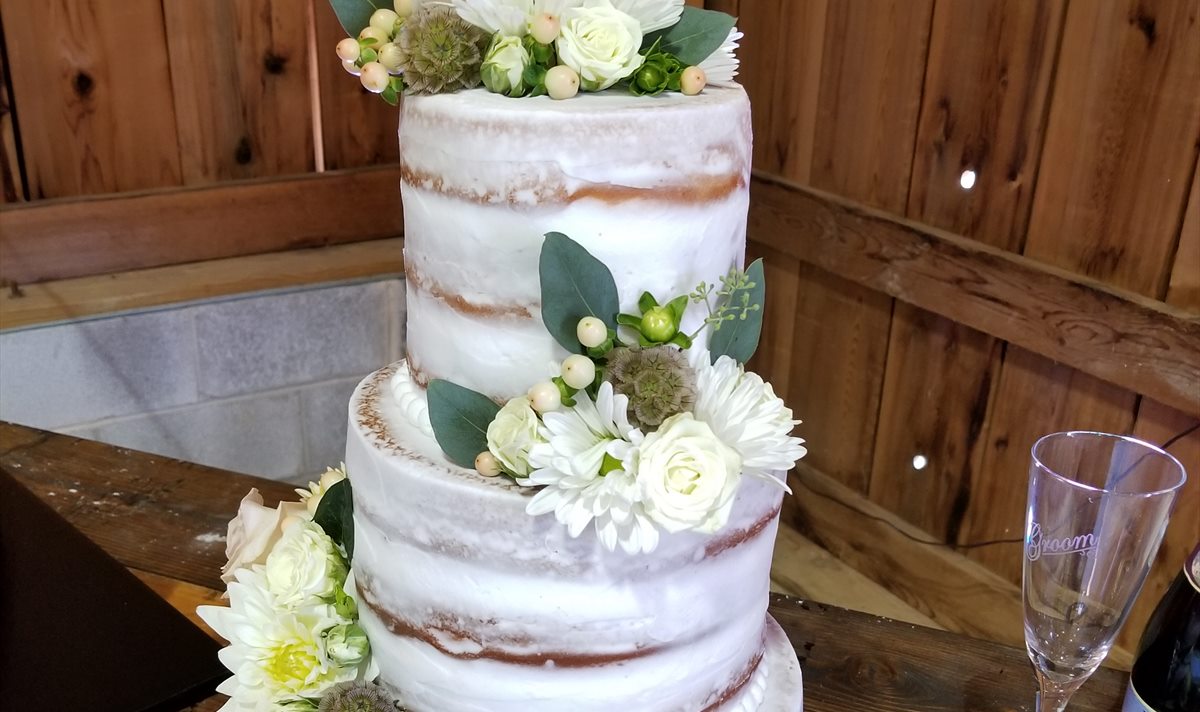 A tiered Sweet Shop wedding cake finished in buttercream and dressed with fresh greenery