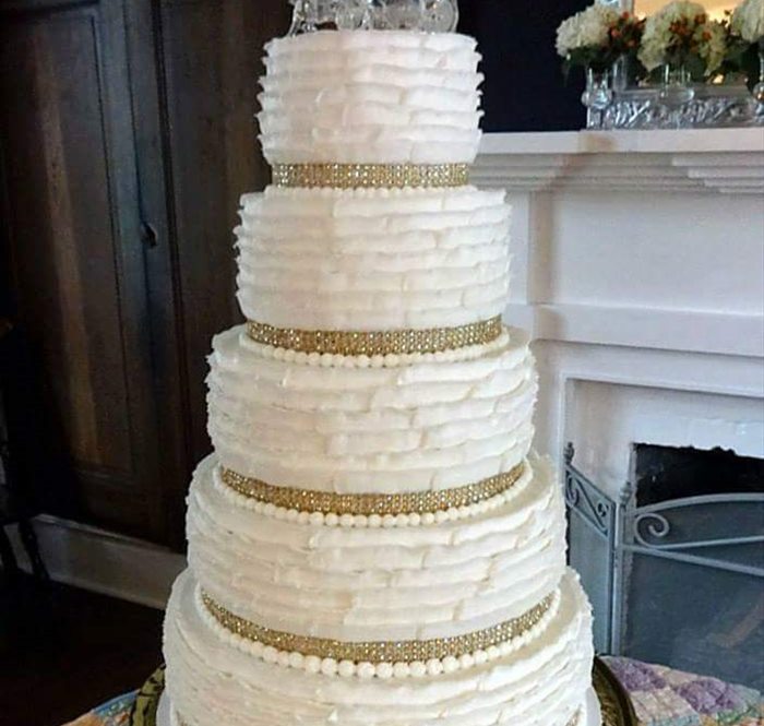 Tiered white wedding cake with lace piping and a gold ribbon