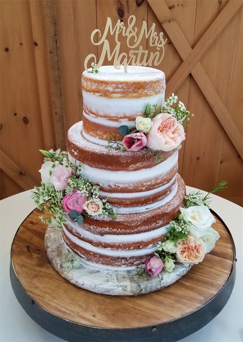 Three-tier semi-naked wedding cake with pink and white flowers on a wood slab