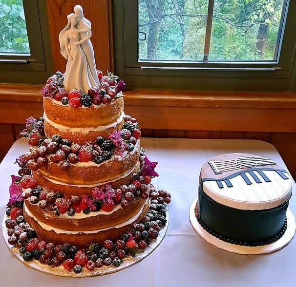 Naked tiered wedding cake topped with fresh berries beside a piano groom cake