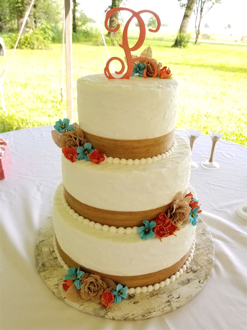 Three-tier buttercream cake with bright flowers and a monogram topper