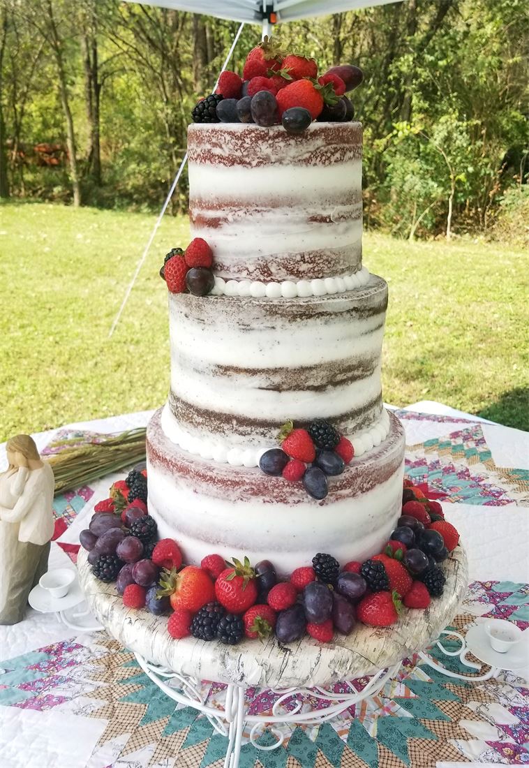 Naked wedding cake with fresh berries on a rustic outdoor table