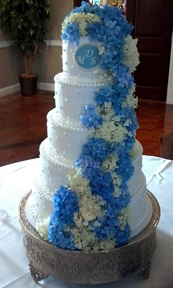 Tall white wedding cake with a blue floral cascade