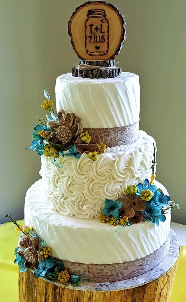 White wedding cake with bright blue and yellow flowers and a monogram topper