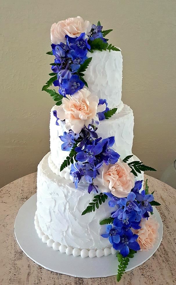 White wedding cake with a cascade of blue and peach flowers